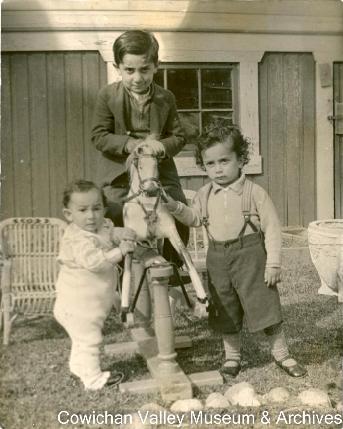 [Rajindi riding a rocking horse next to two young children]