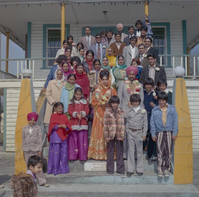 [Photo of an unidentified groom, an unidentified bride and their wedding guests on the Gurdwara steps]