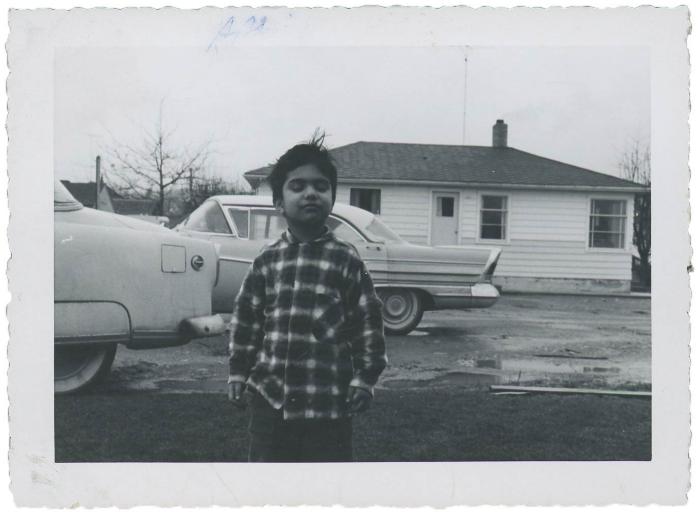 [Photo of Gurmail Singh Gill standing in front of two cars and a house]