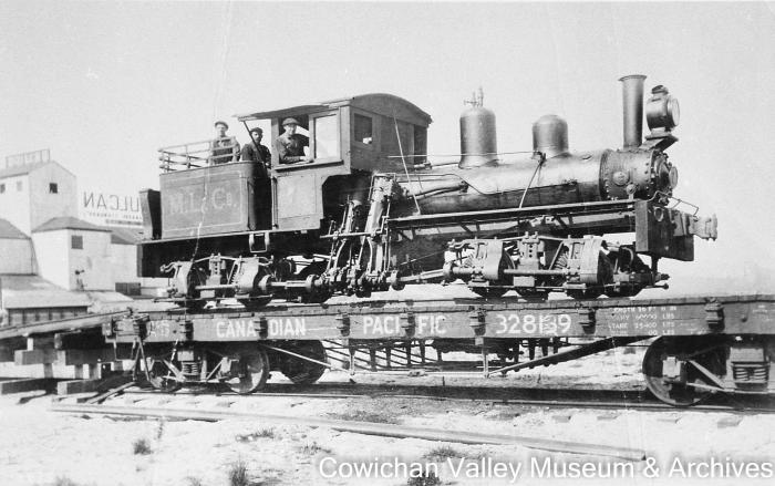 [Three unidentified railroad workers standing on a locomotive loaded on a railcar]